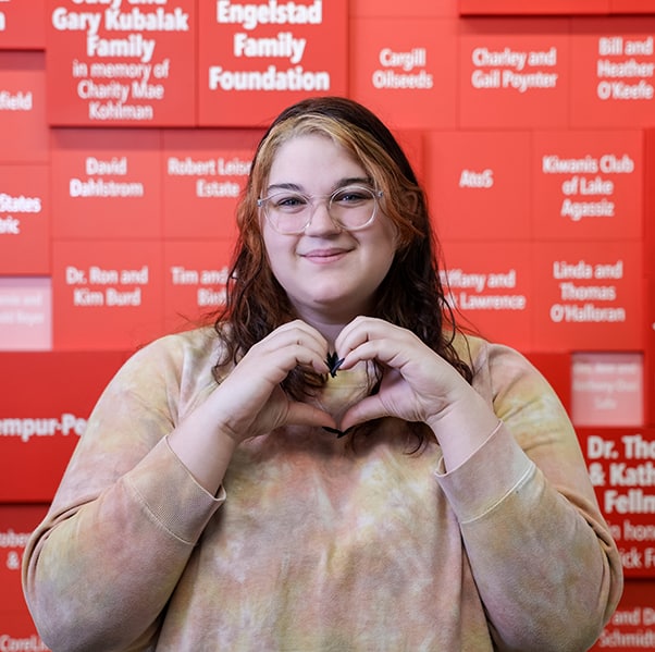 young lady forming a heart with her hands in front of RMHC-RRV donor board